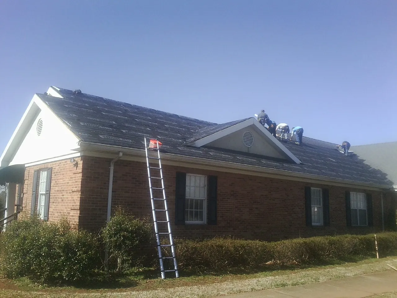 Crew tearing shingles off a brick ranch roof with a ladder set — Emergency Roof Repair work by our crew in Wye Mills