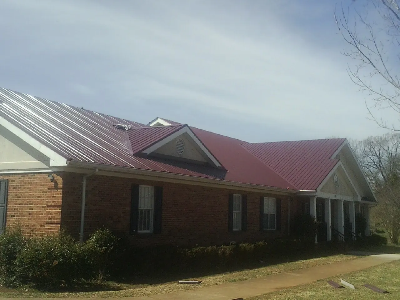Red metal roof with gabled entries on a long brick building, from a Hail Damage Roof Repair job in Wye Mills