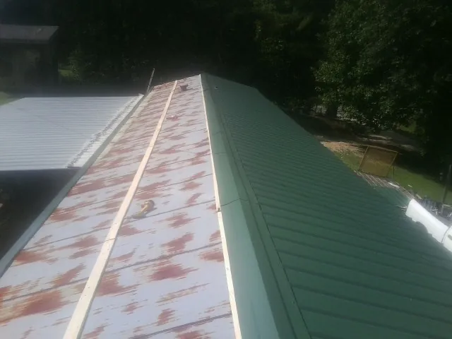 Old rusted panels beside newly installed green metal roofing — Wind Damage Roof Repair by Roofing Brothers in Wye Mills