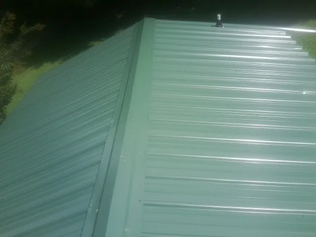 New green metal panels meeting at the ridge of a roof — Flat Roof Repair work by our crew in Wye Mills