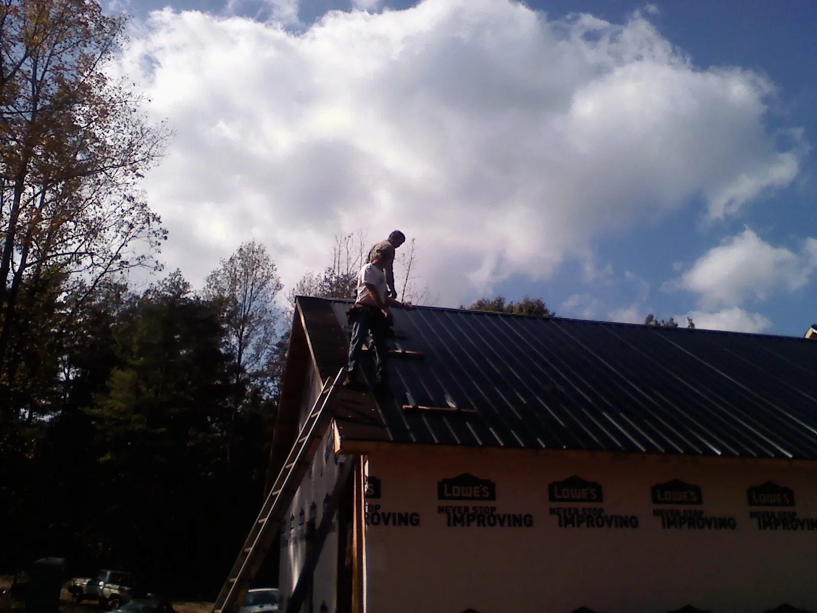 Roofer fastening dark metal panels high against a cloudy sky, from a Roof Inspection job in Wye Mills