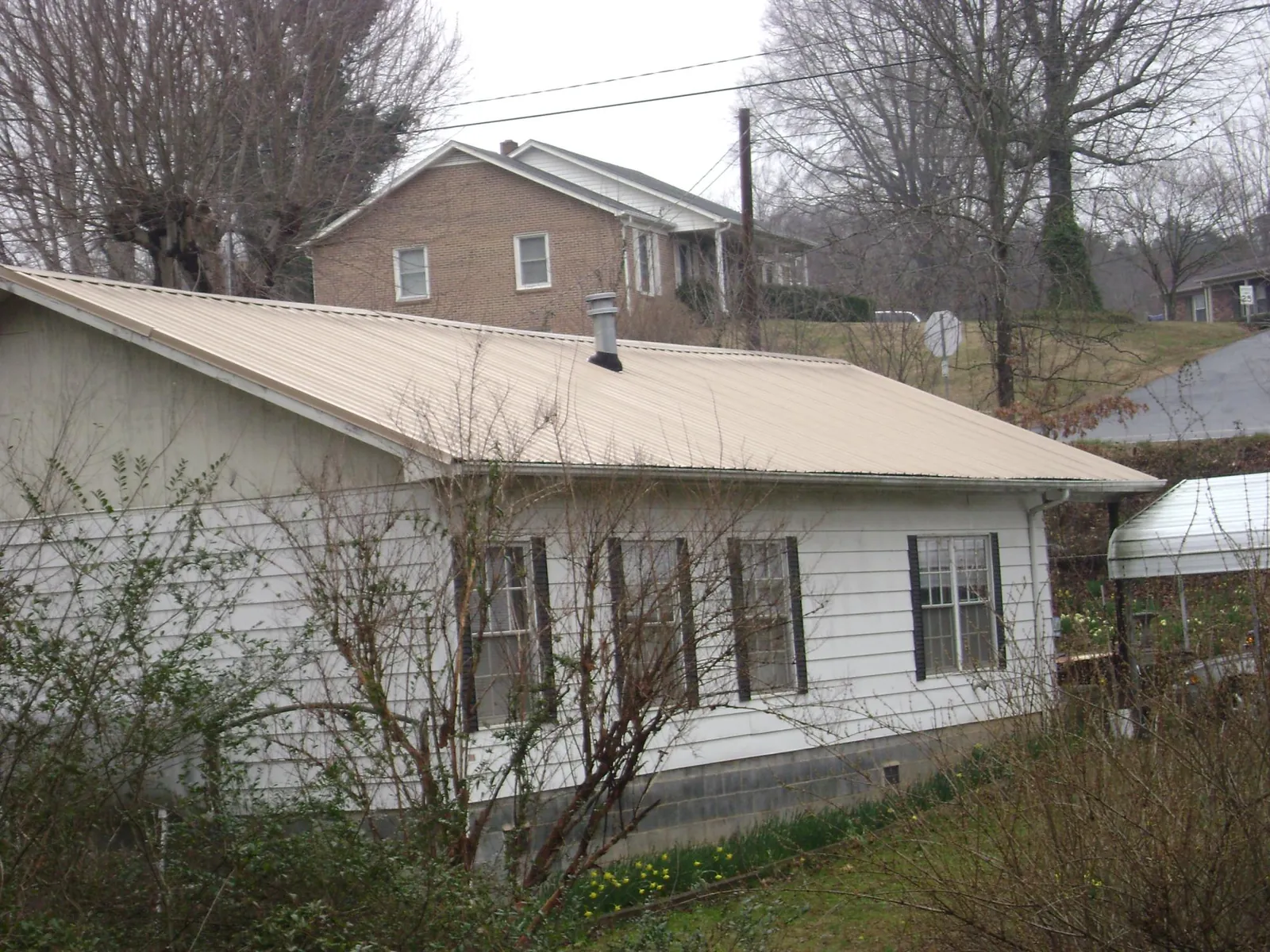 Tan metal roof on a white sided house set into a hillside — Commercial Roofing by Roofing Brothers in Wye Mills
